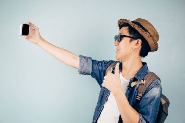 Gülümseyen ve pastel mavi arka plan üzerinde izole bir selfie alarak genç Asya turizm