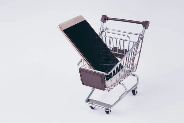 Un carrito de compras con smartphone en el interior, que indica el comercio móvil y el comercio electrónico —  Fotos de Stock