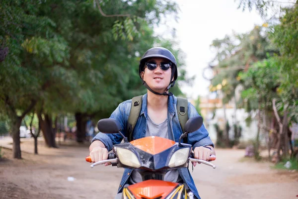 Giovane felice e bello motociclista maschile in occhiali da sole e casco in sella alla moto — Foto Stock