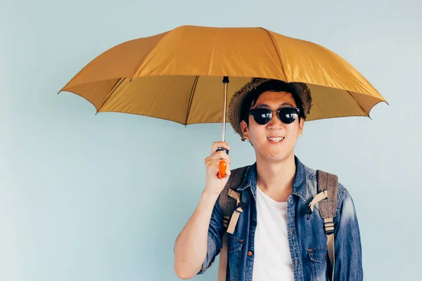Young Asian tourist smiling and holding umbrella isolated over pastel blue background. Alone and Looking for partner to travel