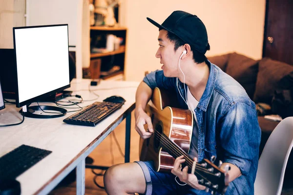 젊은 아시아 남자 컴퓨터 모니터에 기타를 재생 하는 방법을 학습. 남성 기타리스트 보고 온라인 자습서입니다. 모니터에 클리핑 경로 포함 — 스톡 사진