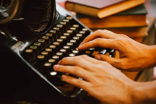 Mãos humanas digitando em máquina de escritor do tipo vintage e pilhas de livros em mesa de madeira foco muito seletivo — Fotografia de Stock