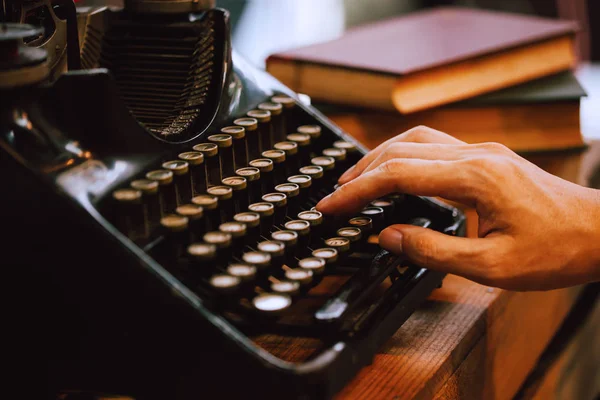 Mãos humanas digitando em máquina de escritor do tipo vintage e pilhas de livros em mesa de madeira foco muito seletivo — Fotografia de Stock
