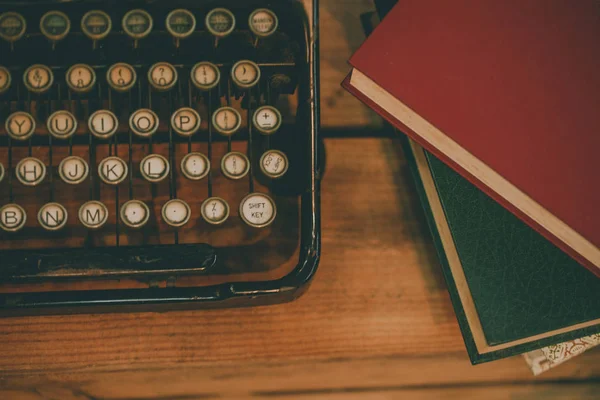 Old and vintage type writer machine and piles of books on wooden table - in vintage tone