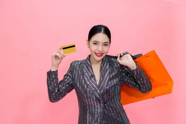 Alışveriş çantaları taşırken ve kredi kartı tutan genç şık Asyalı kadın. Güzel moda kadın pembe arka plan üzerinde izole. Alışveriş ve Finans kavramı — Stok fotoğraf