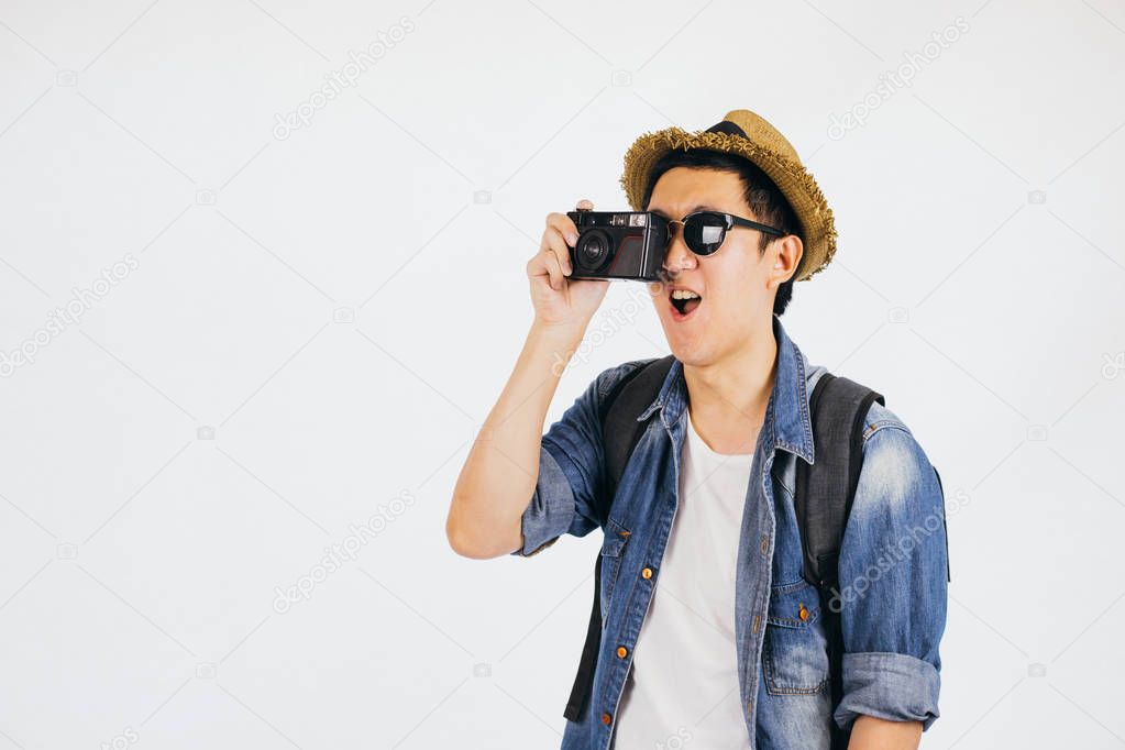 Young Asian tourist with hat and sunglasses smiling and holding camera isolated over white background