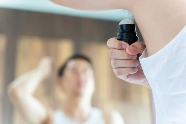 Aziatische guy met behulp van roll op antitranspirant deodorant in badkamer — Stockfoto