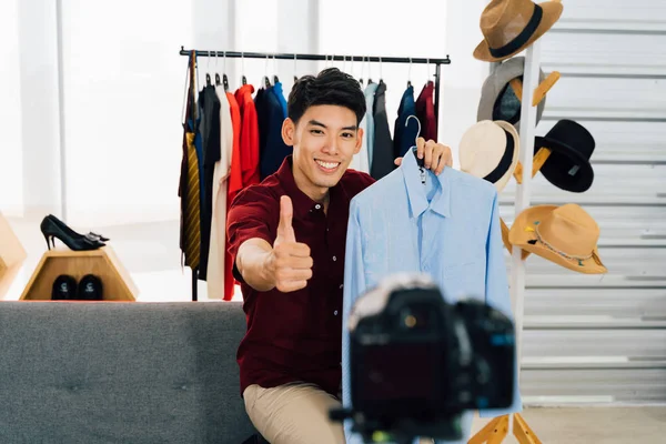 Happy Asian man recording video selling shirt showing thumb up sign