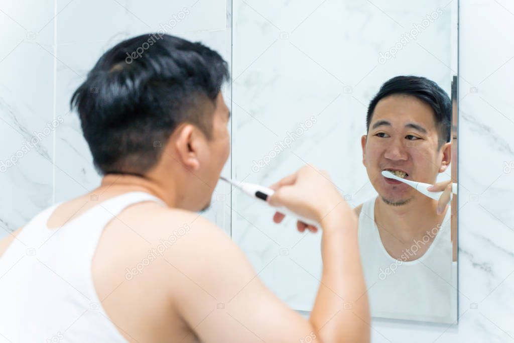 Asian man cleaning teeth using electric toothbrush