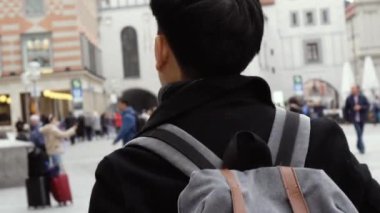 Young Asian man tourist traveling in city centre in Europe. Male backpacker walking in Marienplatz square, Munich, Germany