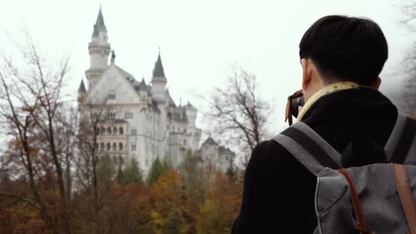 Male Asian tourist with backpack and camera standing and enjoying view of medieval Neuschwanstein castle — Stok video