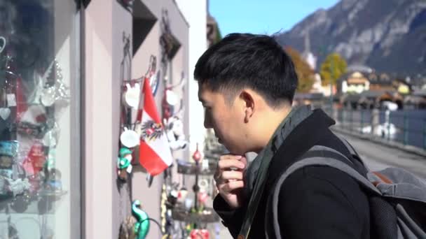 Mladý asijský muž turistických nákupů a při pohledu na suvenýry v Hallstatt Lake v Salzkammergut během cesty do Rakouska — Stock video