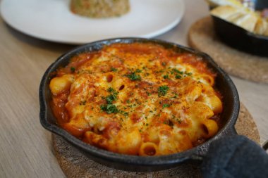 Macaroni mixed with cheese and tomato sauce served on pan