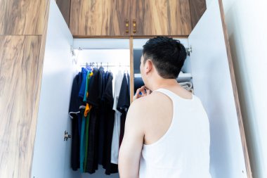 Güneşli bir günde evde kıyafet seçen bir adam.