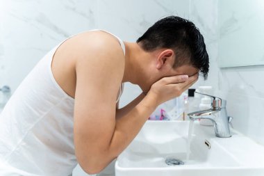Young guy cleaning face above sink in bathroom
