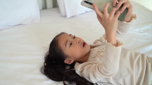 Kalm aziatisch kind spelen spel op mobiele telefoon liggend op bed — Stockvideo