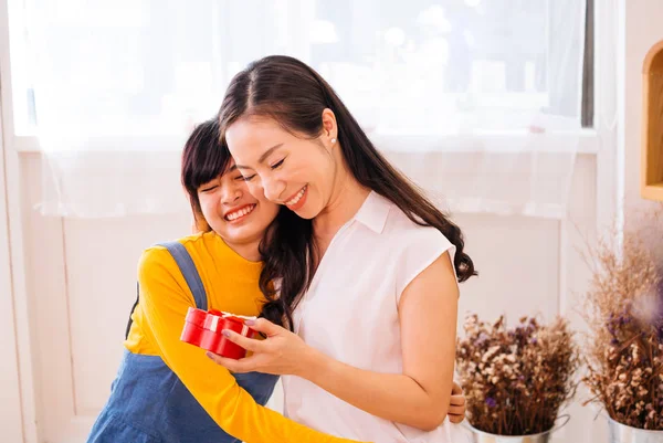 Sonriendo feliz hija adolescente asiática y madre de mediana edad asiática abrazándose juntos en la sala de estar cubierta en casa — Foto de Stock