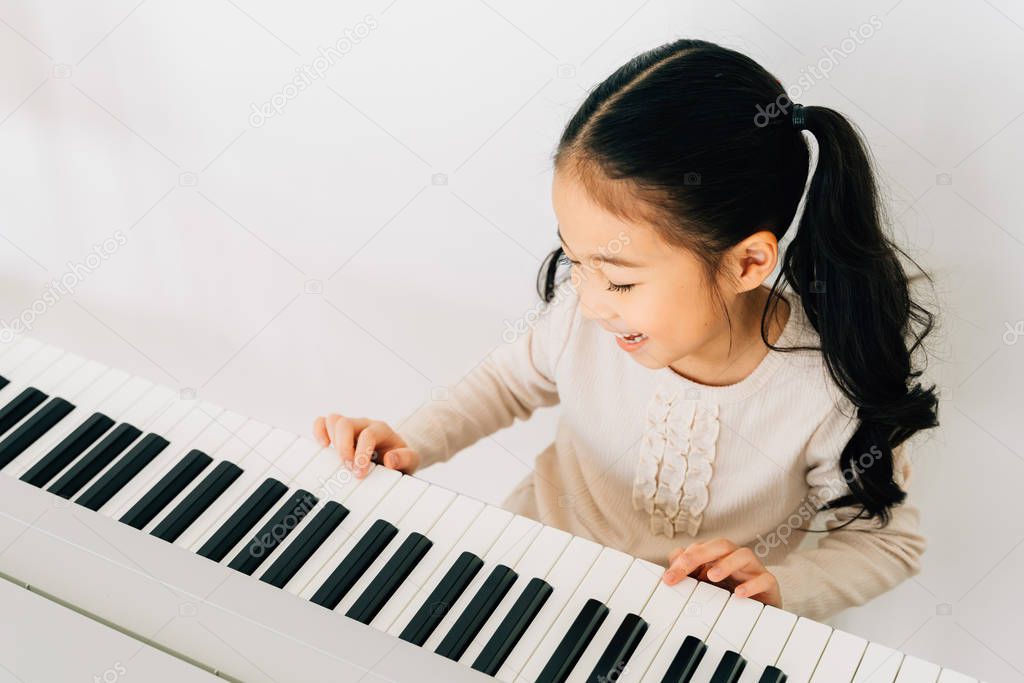 Satisfied Asian kid playing piano at home