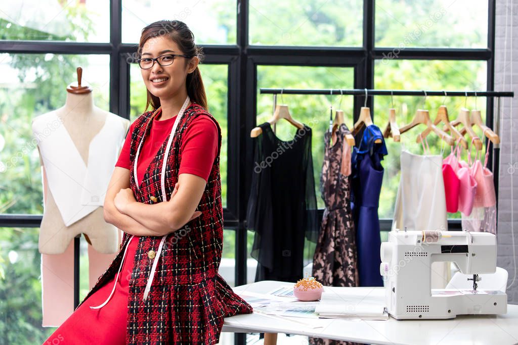 Young Asian fashion designer smiling and looking at camera in front of working desk