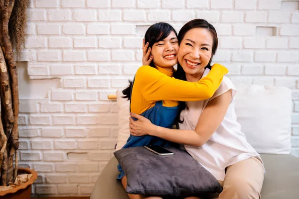 Веселая азиатская мать и дочь обнимаются, сидя на диване — стоковое фото