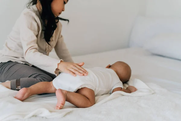 Serious Asian kid patting infant lying on bed — 스톡 사진