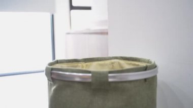 Young man putting clothes in laundry basket at home with window and walking to clean it