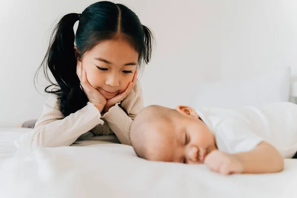 Asian family of cute little sister touching newborn baby boy brother. Toddler kid and new sibling relax in a white bedroom at home — 스톡 사진