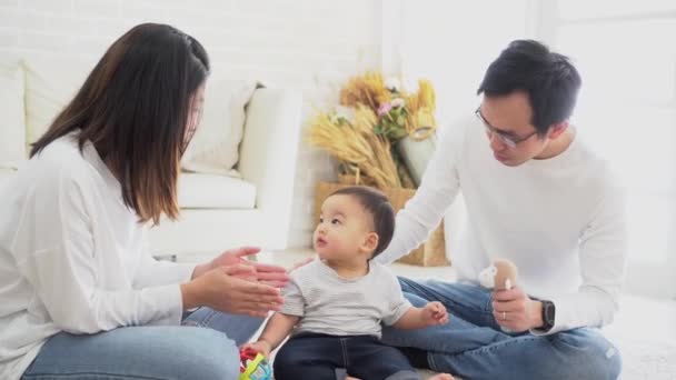 Азиатская семья отца и матери играют в игрушечную куклу со своим сыном на полу дома — стоковое видео