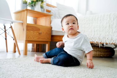 Asian boy sitting on the floor alone at home next to bed