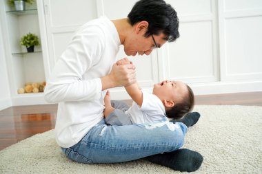 Happy Asian father with his little baby boy son playing in living room, enjoying family time