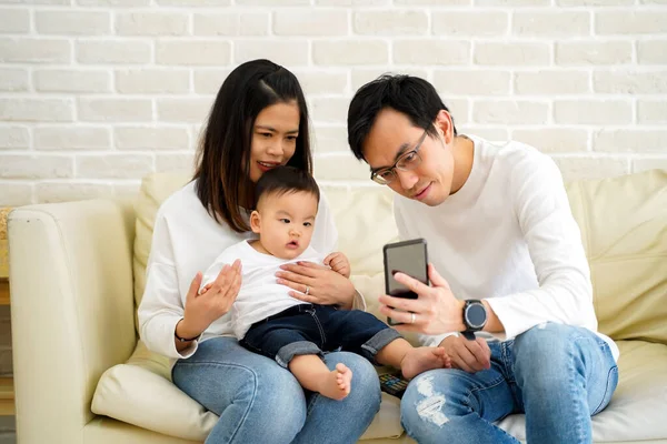 Allegro giovane famiglia asiatica con figlio a guardare video sul telefono cellulare e seduto sul divano divano a casa — Foto Stock