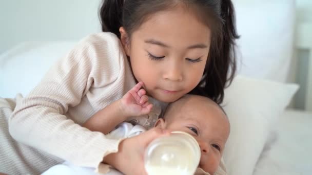 Asijské rodina roztomilé dívka sestra krmení mléko z láhve pro její novorozený bratr a ležící na posteli — Stock video