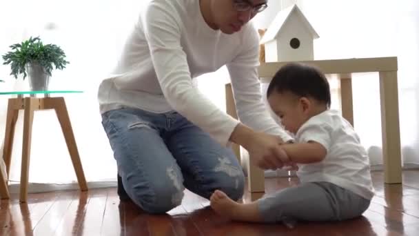 Serious Asian little boy crawling on floor while young father sitting next to him in living room — 图库视频影像