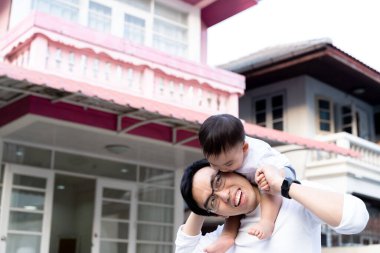 Asian father giving a piggyback ride for little son in front of the house