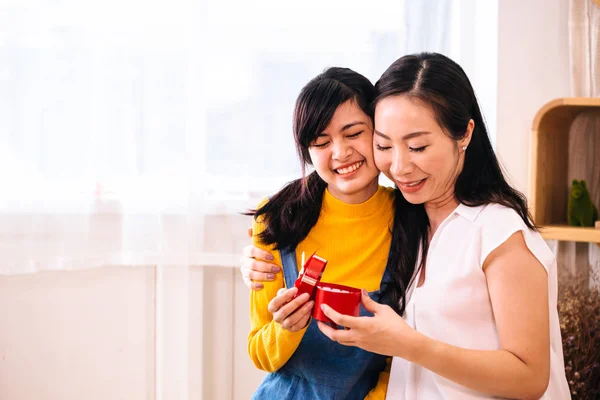 Улыбаясь счастливая азиатская дочь-подросток и азиатская мать среднего возраста обнимаются в закрытой гостиной дома — стоковое фото