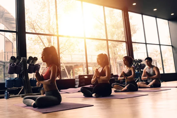 Bir grup Asyalı kadın ve erkek aerobik dersinde yoga minderlerinde pilates yapıyorlar. Genç sporcular bacak bacak üstüne atarak spor salonunda poz veriyorlar.. — Stok fotoğraf