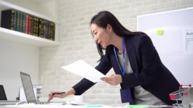 Ofis masasının başında duran Asyalı iş kadını belgeleri gözden geçiriyor.