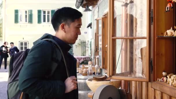 Молодой азиат покупает туристические товары и смотрит на сувениры в озере Халлстатт в Зальцкаммергуте во время поездки в Австрию — стоковое видео