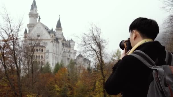 Male Asian tourist with backpack and camera standing and enjoying view of medieval Neuschwanstein castle — Stok video