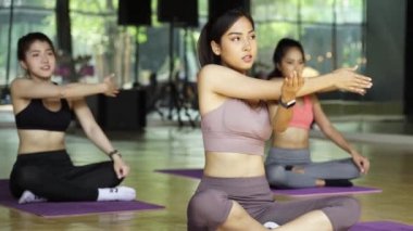 Bir grup Asyalı kız spor salonundaki aerobik fitness sınıfında yoga esneme pozisyonu alıyorlar. Yoga minderinde bacak bacak üstüne atan mutlu genç sporcular..