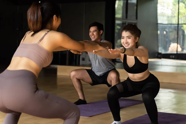 Grupa szczęśliwych Azjatek i mężczyzn robiących przysiady na matach do jogi w klasie aerobiku. Młodzi sportowcy uśmiechnięci podczas treningu w studio fitness. — Zdjęcie stockowe