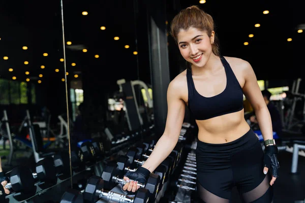 Uśmiechnięta azjatycka atletyczna kobieta patrzy w kamerę podczas treningu z dumbells na siłowni. — Zdjęcie stockowe