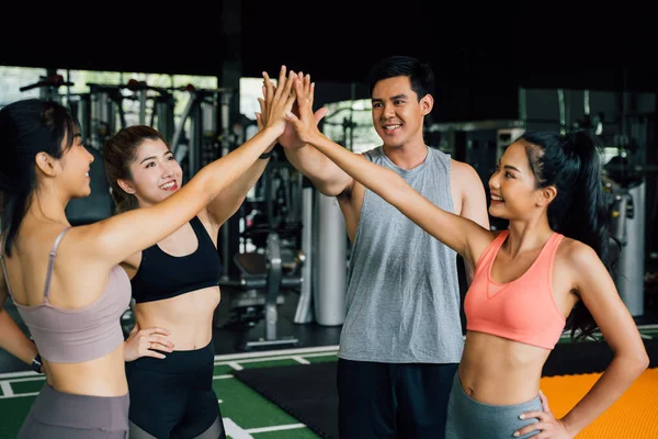Улыбающиеся мужчины и женщины делают вместе руки в фитнес-зале. Группа молодых людей делает пять жестов в спортзале после тренировки. Счастлив успешным занятием после тренировки. Концепция командной работы. — стоковое фото