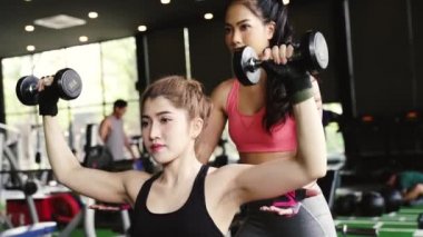 Spor salonunda ağırlık kaldırma egzersizini yapması için vücut geliştiren bir kadına antrenörlük yapan Asyalı bir antrenör.. 