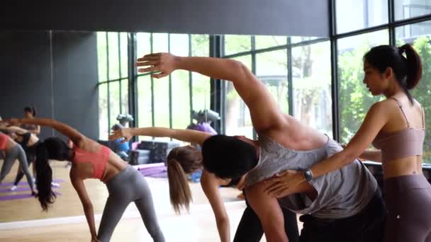 Aziatische jonge yoga vrouwelijke instructeur het helpen van een mannelijke beginner balanceren flexibiliteit poseren in de klas in sportschool studio. Yoga en pilates klaslokaal in Azië — Stockvideo