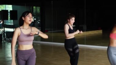 Beden eğitimi stüdyosunda Latin dansı dersi alan kadın fitness kadınları. Bir grup genç sporcu kadın ellerini havaya kaldırıyor.