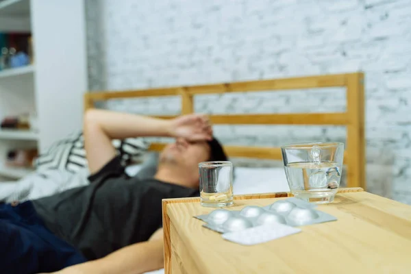 Young Asian man feeling sick and ill lying on bed with medicines tablets and pills on table — Stock Photo, Image