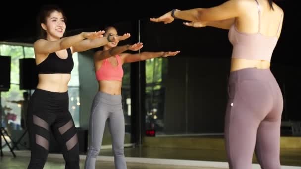 Grupp glada asiatiska kvinnor och man gör squat övningar på yogamatta i aerobics klass. Unga sportiga människor ler när du tränar i gym studio — Stockvideo