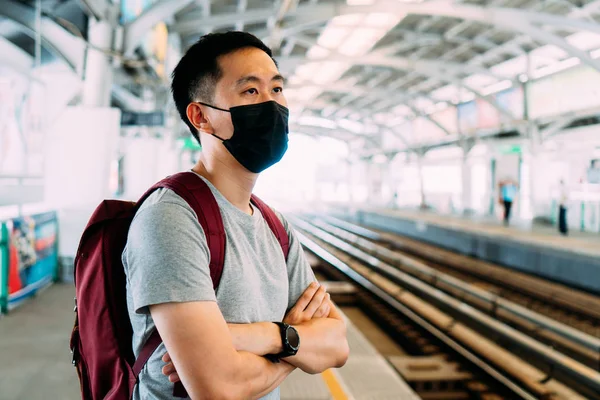 Close up de um jovem asiático vestindo uma máscara facial cirúrgica preta esperando o trem durante o novo tipo Coronavirus Covid-19 surto de pneumonia e pm 2,5 smog crise de poluição do ar na cidade grande — Fotografia de Stock