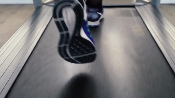 Афроамериканский спортсмен в синих кроссовках работает на электрической беговой дорожке в фитнес-клубе. Безликий бегун на беговой дорожке — стоковое видео